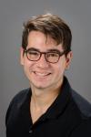Photograph of Pedro Abelin's face. Pedro is a young Latino with brown hair. He is wearing a black shirt and brown sunglasses.