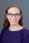 Headshot. Women with purple blouse and glasses on grey background. 