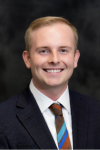 A man in a suit and tie smiles confidently in a professional photo