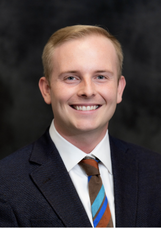 A man in a suit and tie smiles confidently in a professional photo