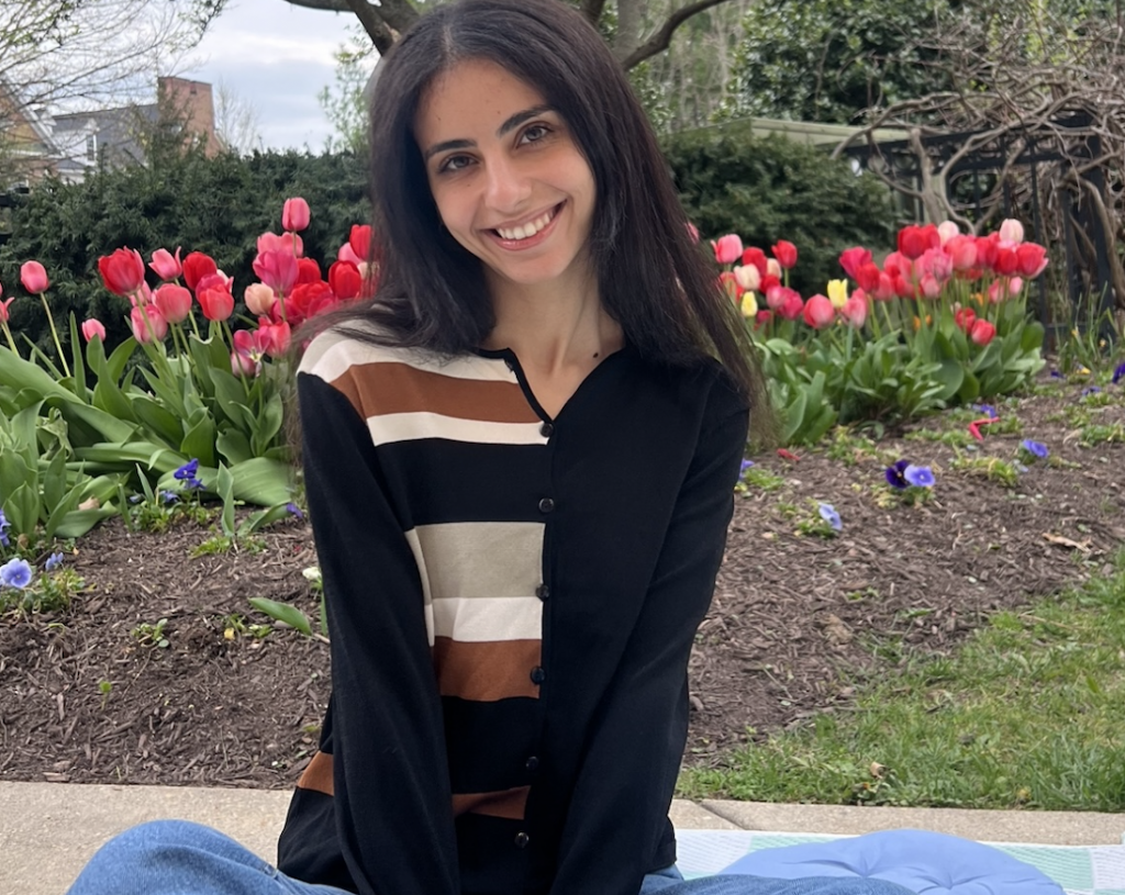 Salma sits cross legged on a lawn, smiling into the camera.